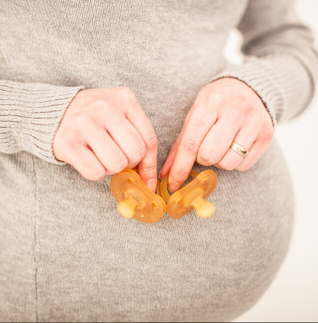 woman pregnant with twins holding two pacifiers 